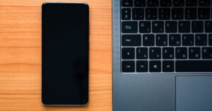 Smartphone and laptop side by side on a desk, representing two booking platforms kept in sync