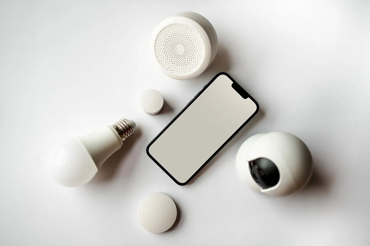A flat lay of a phone, a smart bulb and small sensors on a white surface