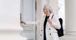 An older woman in a white coat opening the front door of a house