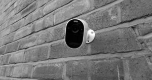A white wireless security camera mounted on a grey brick exterior wall
