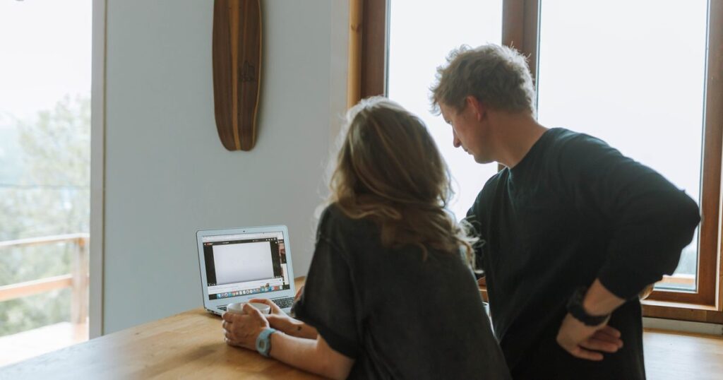 Two people standing at a kitchen counter looking at a laptop together