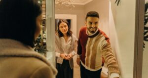Two guests arriving at an apartment door while the host holds it open