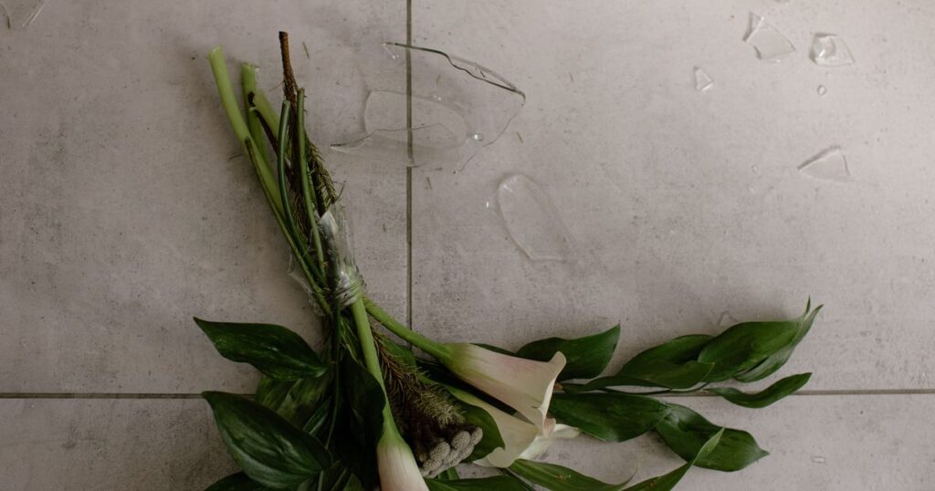 Calla lilies and broken glass from a vase on a tiled floor