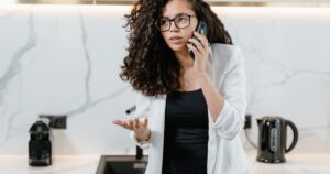 A woman on the phone in a kitchen, one hand raised mid-explanation