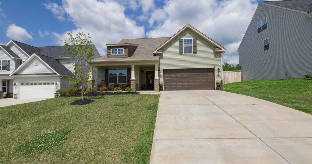 A two-storey suburban house with a long concrete driveway and a green lawn
