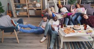 Friends asleep on a sofa and the floor after a birthday party, pizza and cake on the table
