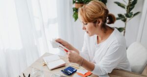 A woman at a desk looking over receipts next to a calculator and a laptop