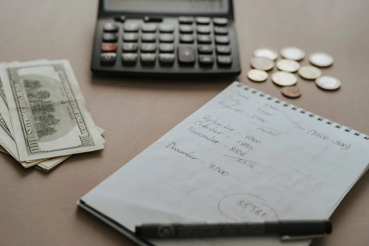 A notebook with a handwritten month-by-month list of figures beside a calculator