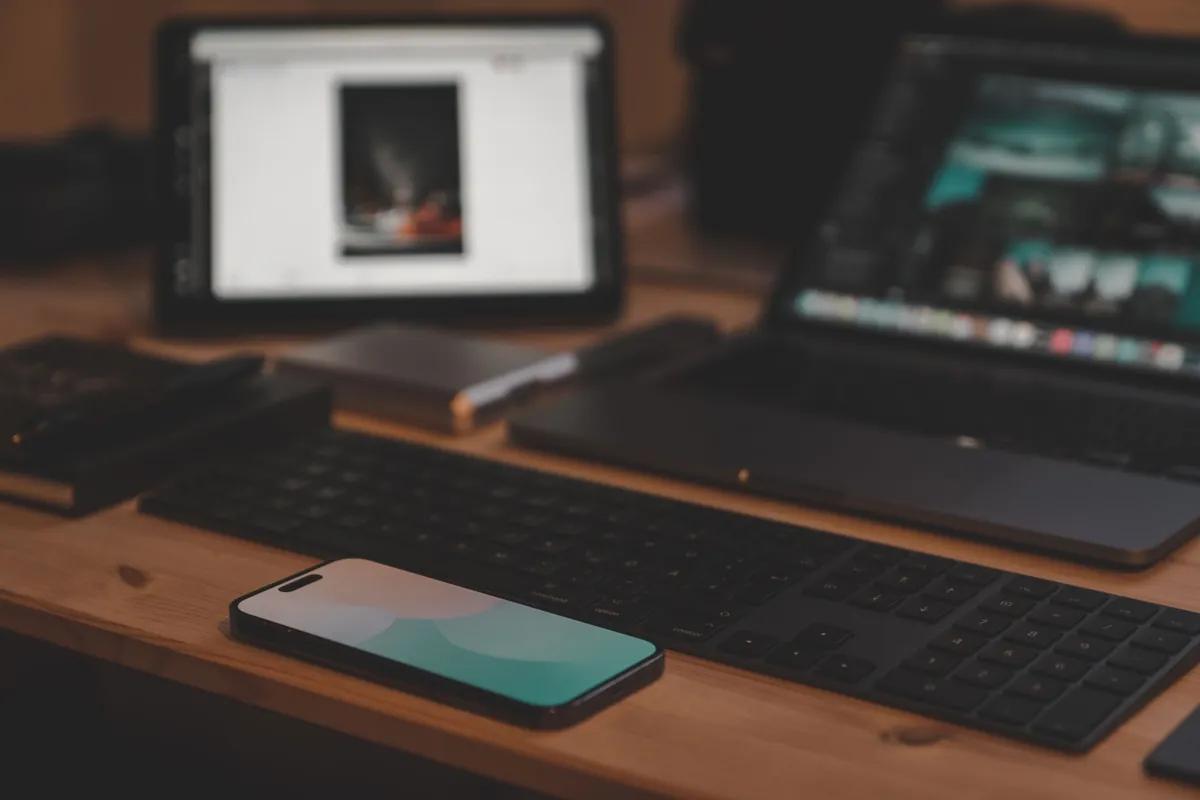 A tablet, a laptop, a keyboard and a phone together on a wooden desk