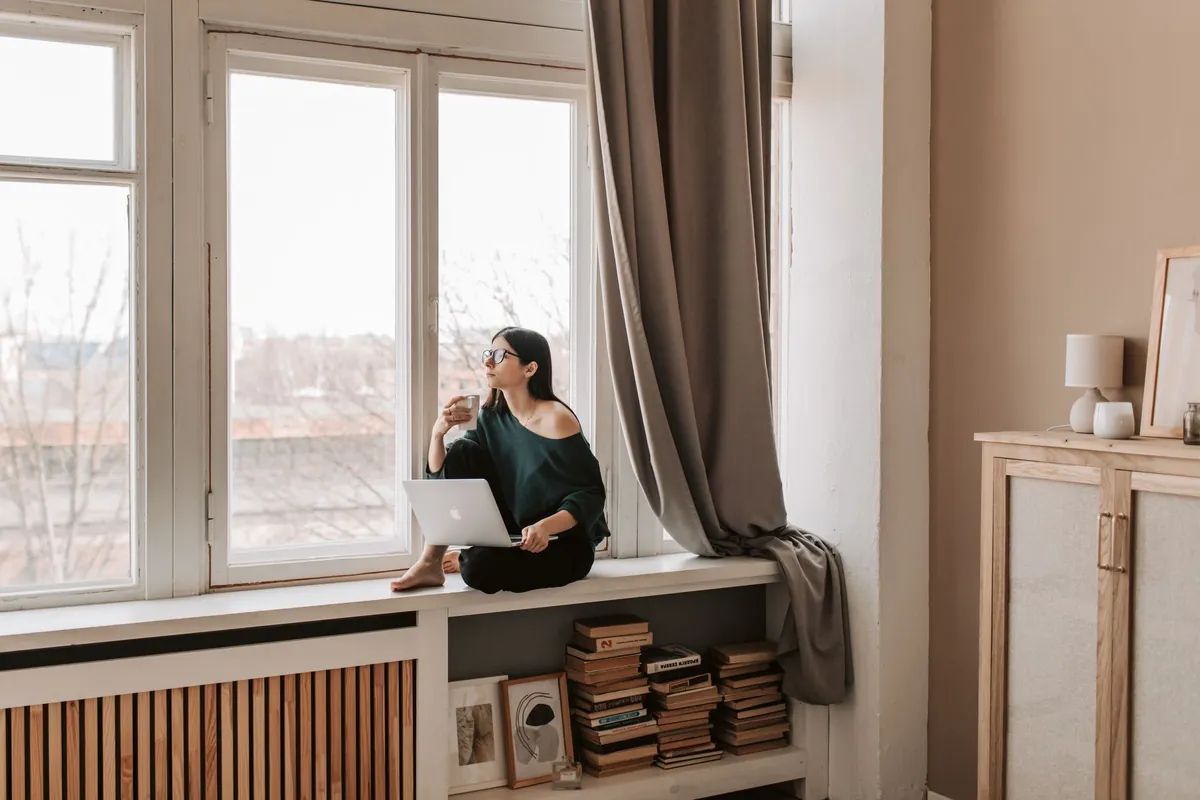 A person sitting on a window seat with a hot drink, looking out at the rooftops