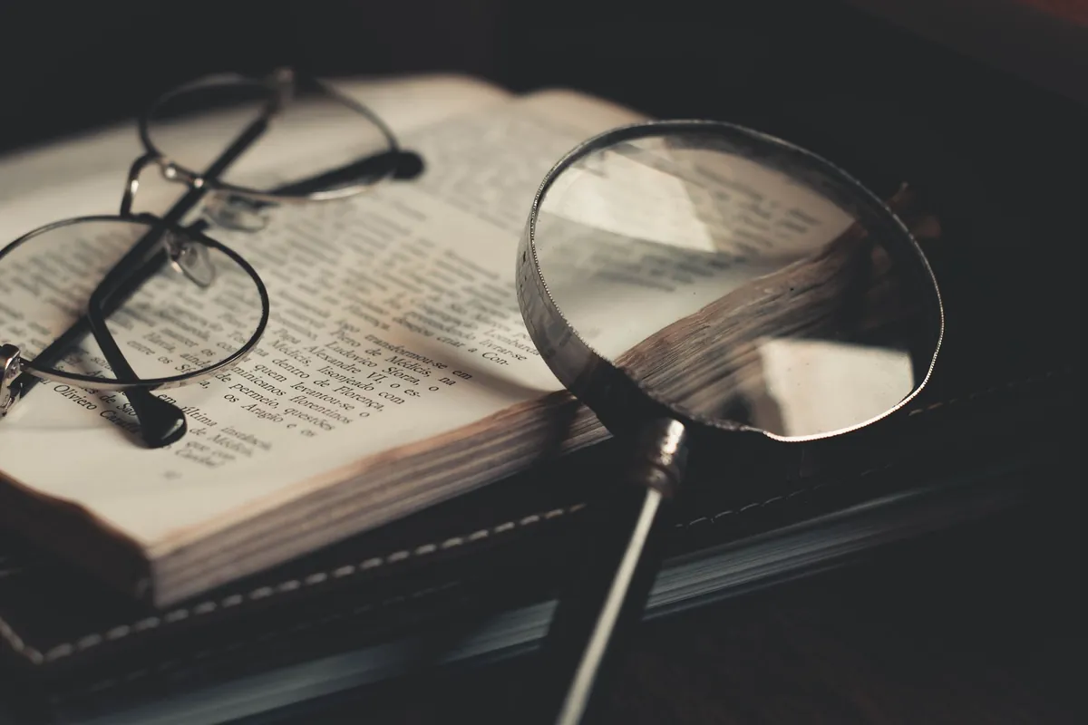 An open book under a magnifying glass on a wooden table