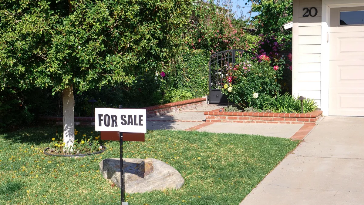A For Sale sign in front of a house with a mature tree and a garden path