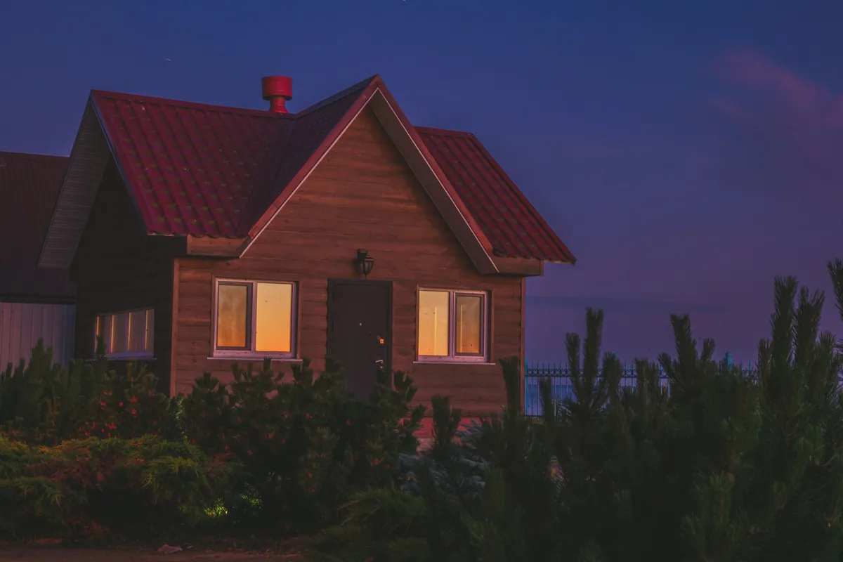 A wooden cabin lit from inside at twilight, surrounded by trees