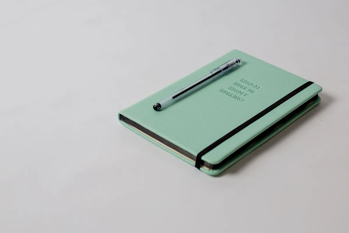 A closed dark green notebook with a pen resting on its cover