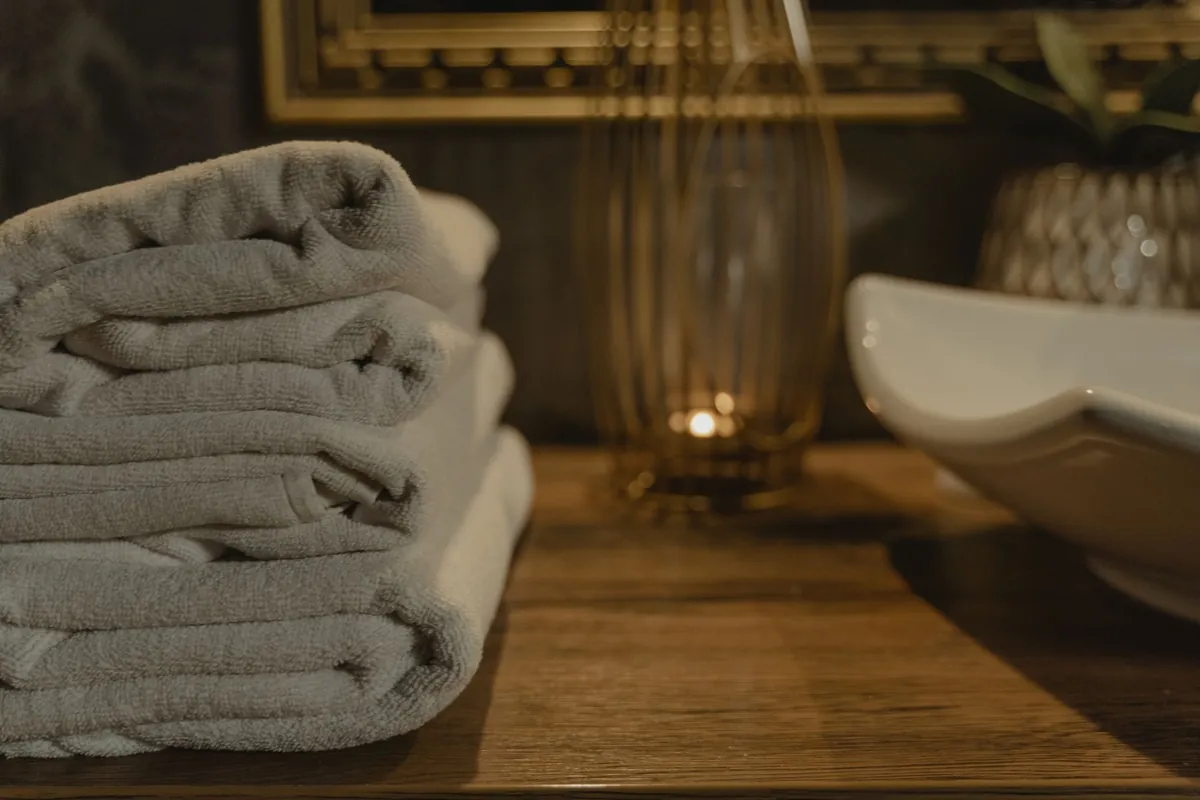 A stack of folded grey towels on a wooden surface beside a basin