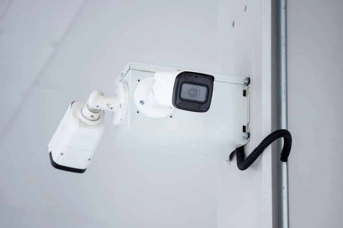 A white bullet security camera fixed to an exterior wall with its cable showing