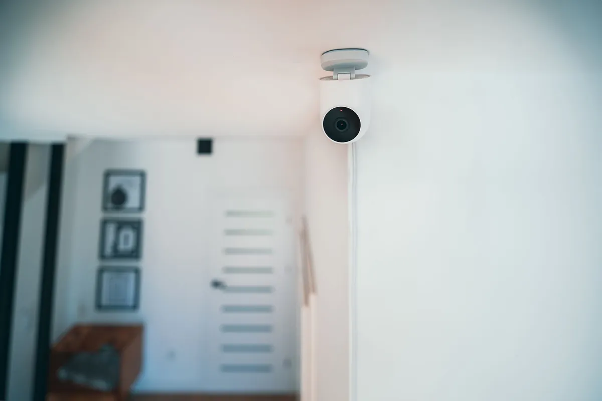 A small camera mounted high on a white wall inside a home hallway
