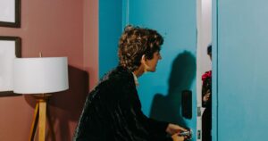 A person unlocking a teal front door while someone waits inside