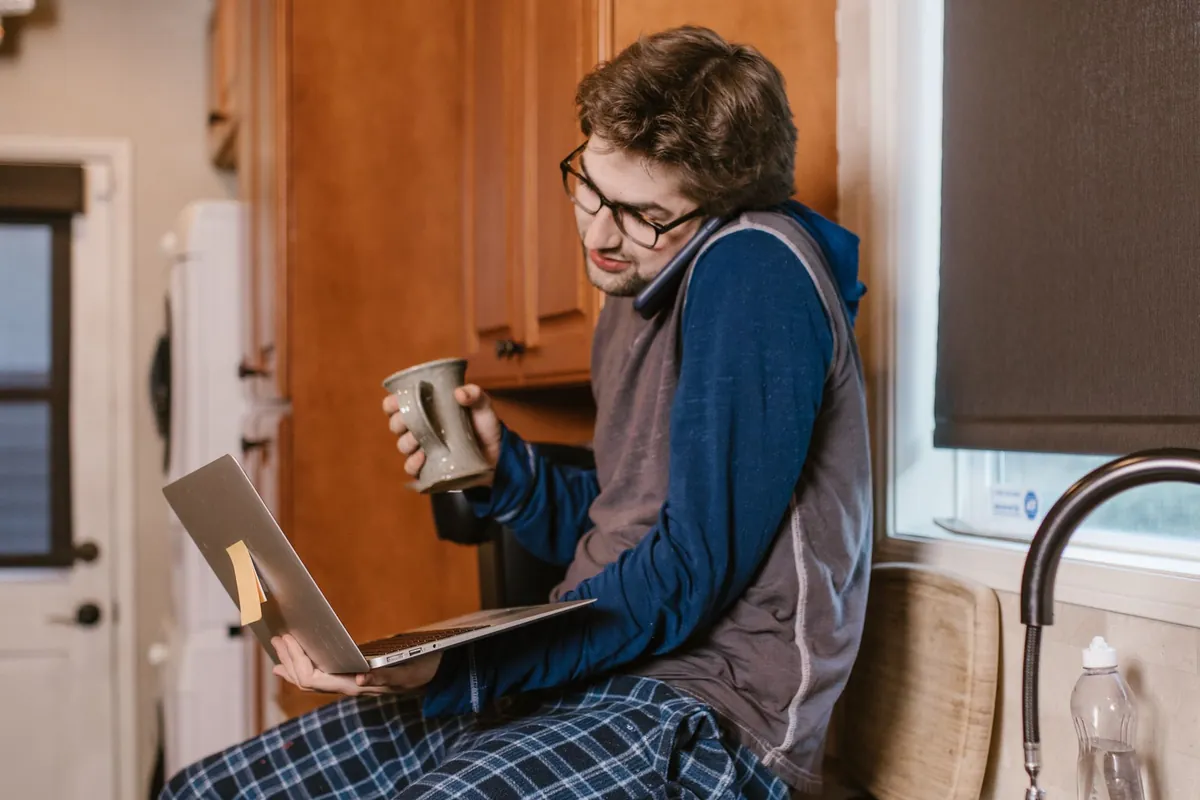 A man in a kitchen reading a laptop, a mug in his hand