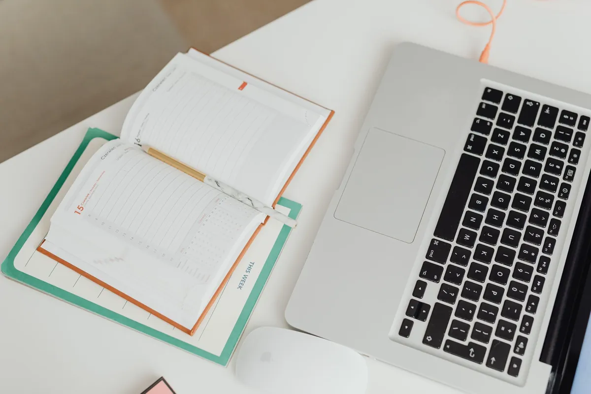A tidy desk photographed from above with an open laptop, a blank notebook and a mouse