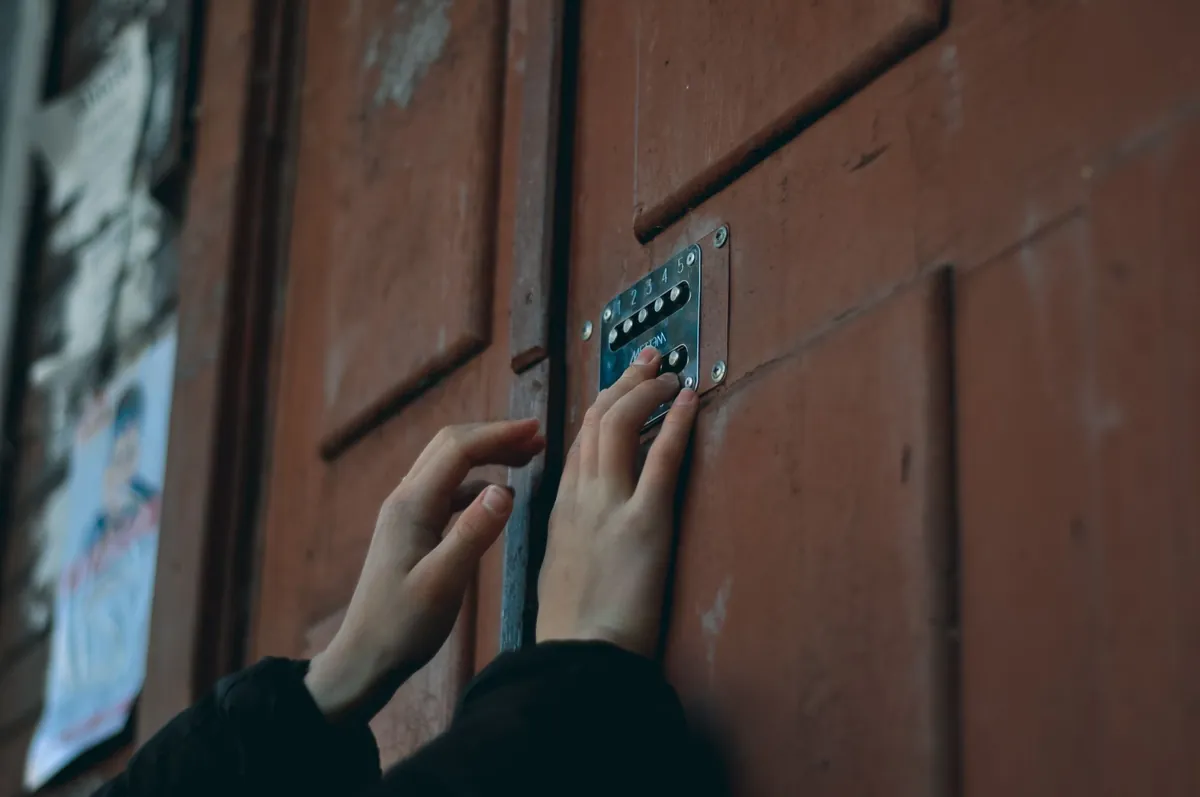 A hand entering a code on a keypad beside a wooden door