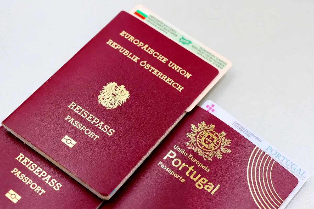 Two closed burgundy passports and the edge of a national ID card fanned out on a plain pale grey surface.