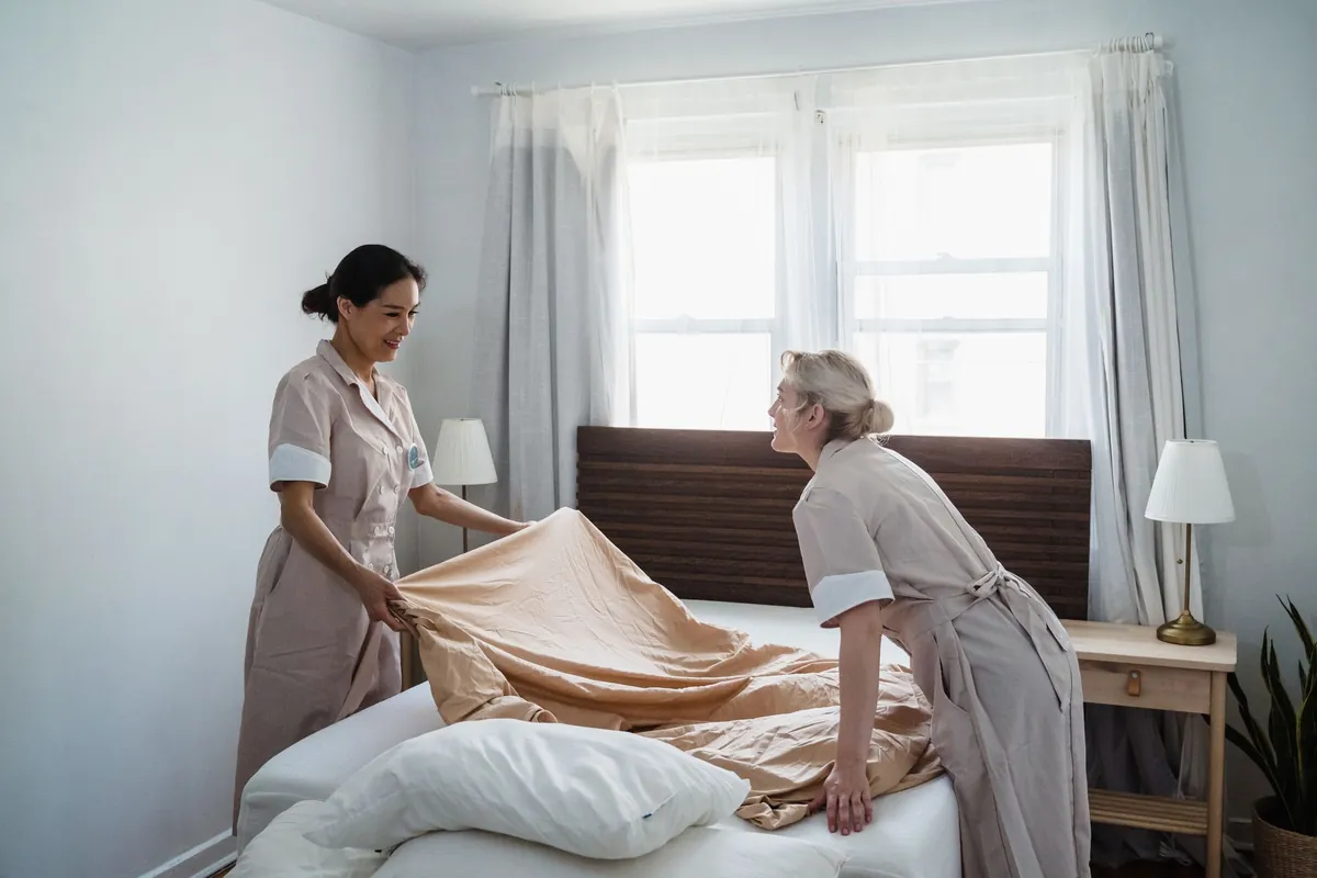 Two housekeepers in uniform making a bed together in a bright bedroom