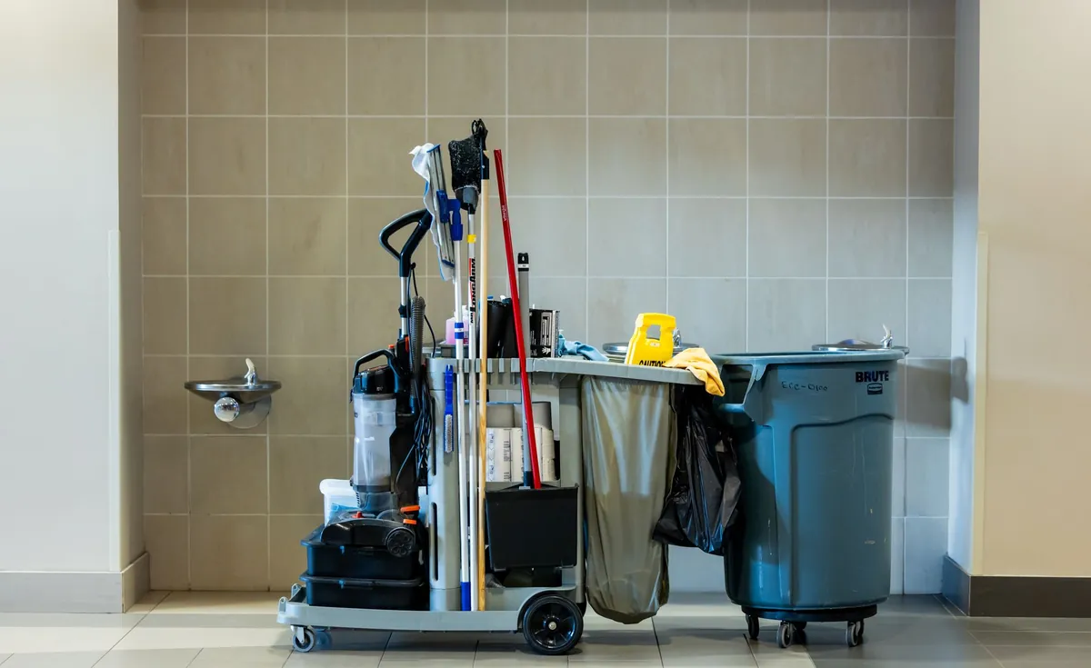 A loaded professional cleaning cart standing in a tiled corridor
