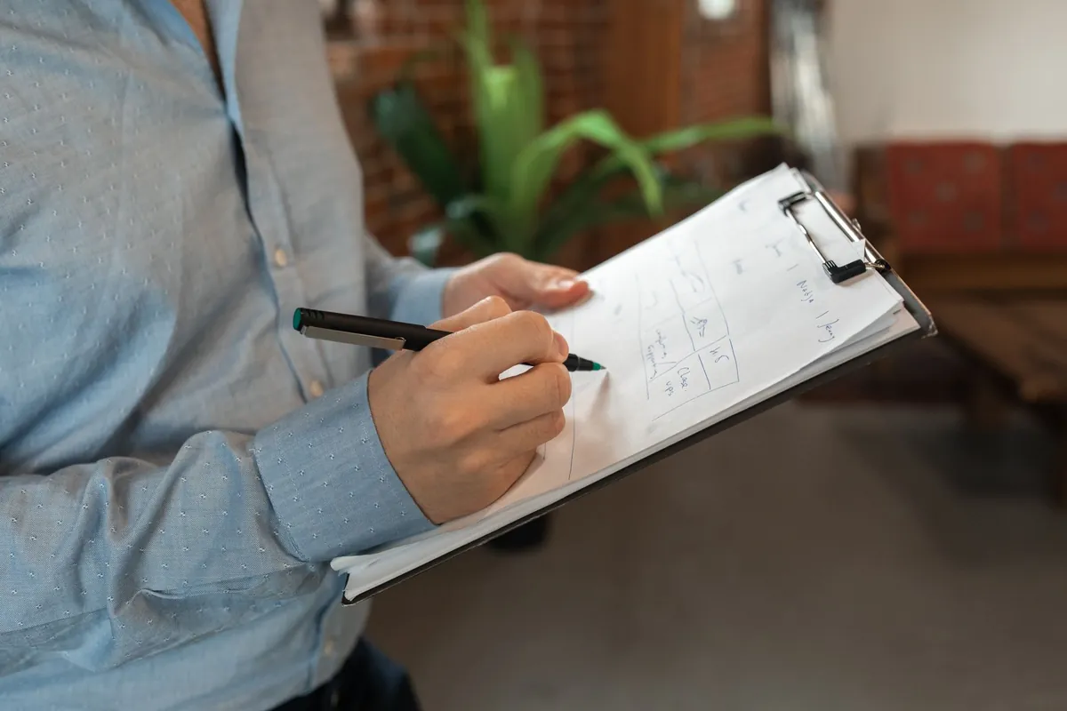 A person writing on a clipboard held against their arm