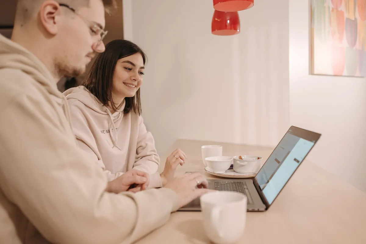 Two people sitting side by side at a table working on one laptop
