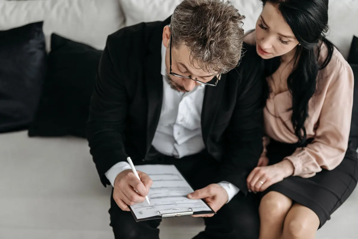 Two people leaning over a printed form together, one holding a pen