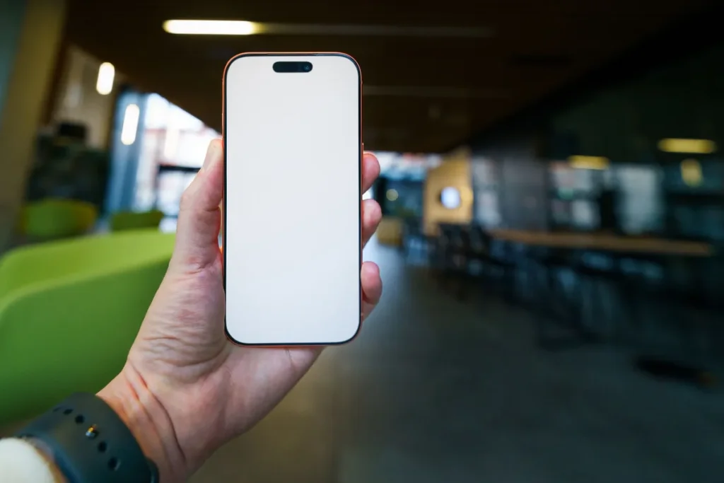 A hand holding a phone with a blank screen in a bright open lobby