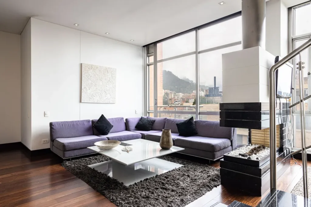 A living room with a purple sectional sofa and a window onto the city