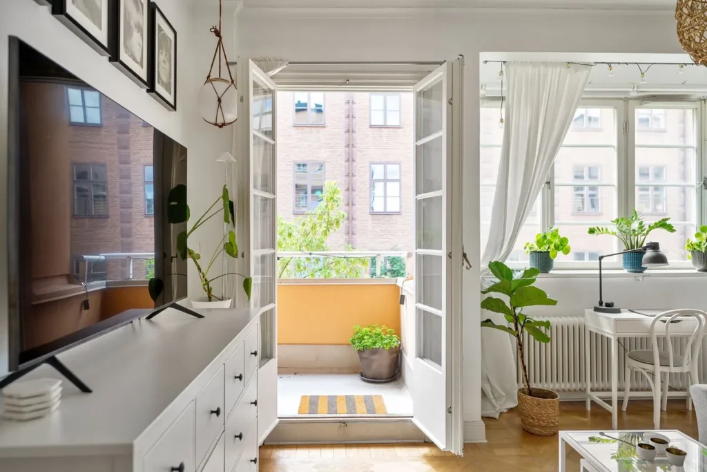 A Scandinavian living room with French doors open onto a sunlit balcony