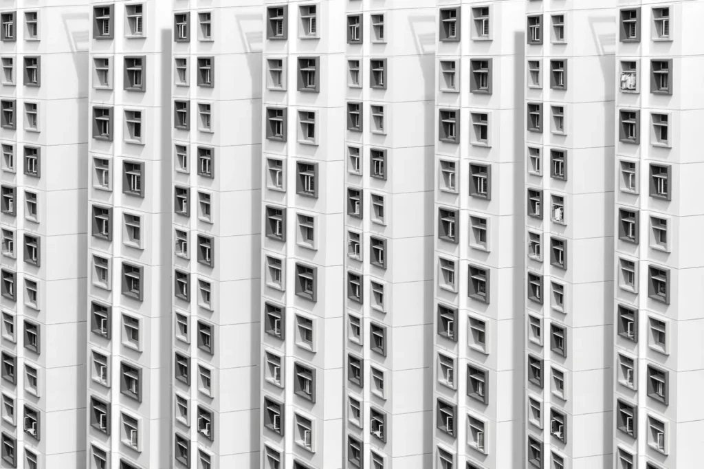 A high-key white residential tower facade filling the frame with repeating rows of recessed windows and balcony boxes.