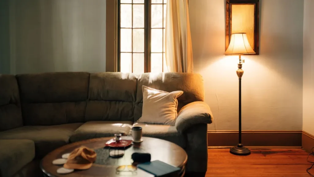 A lived-in living room in the evening with a floor lamp lit beside a sofa and a coffee table holding a mug and a pair of glasses