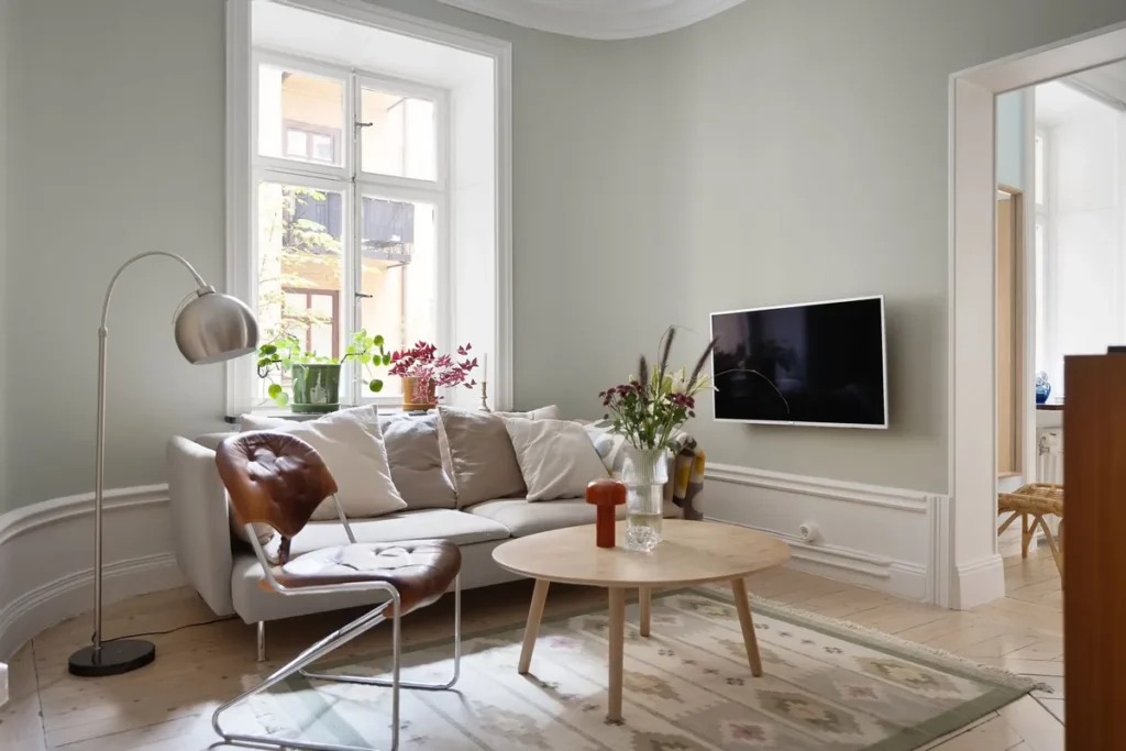 A bright living room with a white sofa, a leather chair and a round wooden table