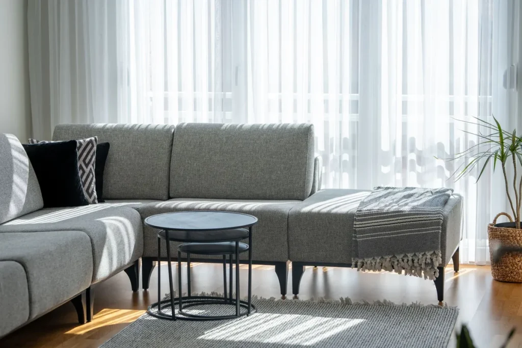 A grey sectional sofa in a sunlit room behind sheer curtains