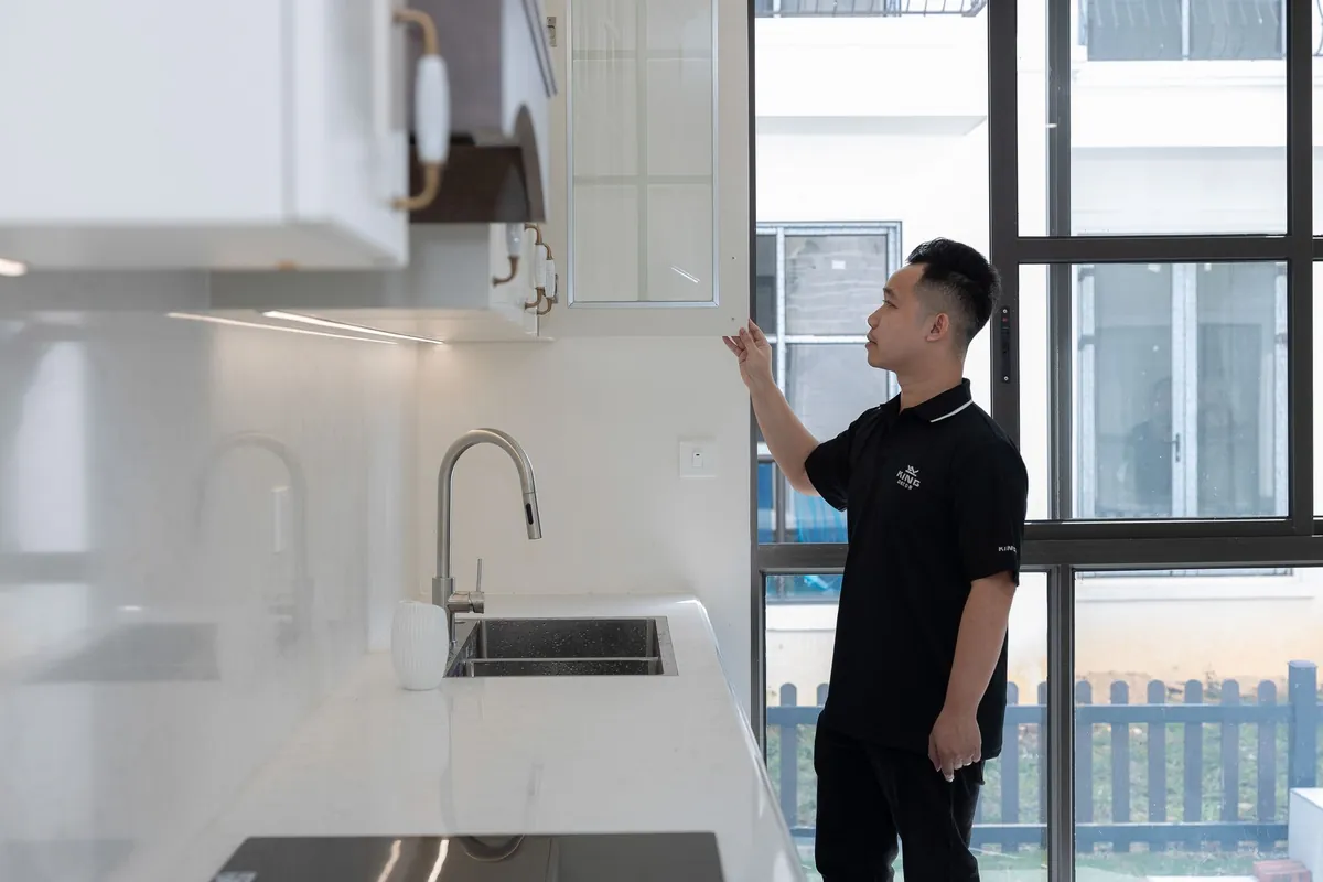 A man in a dark polo shirt checking an open cabinet above a kitchen counter