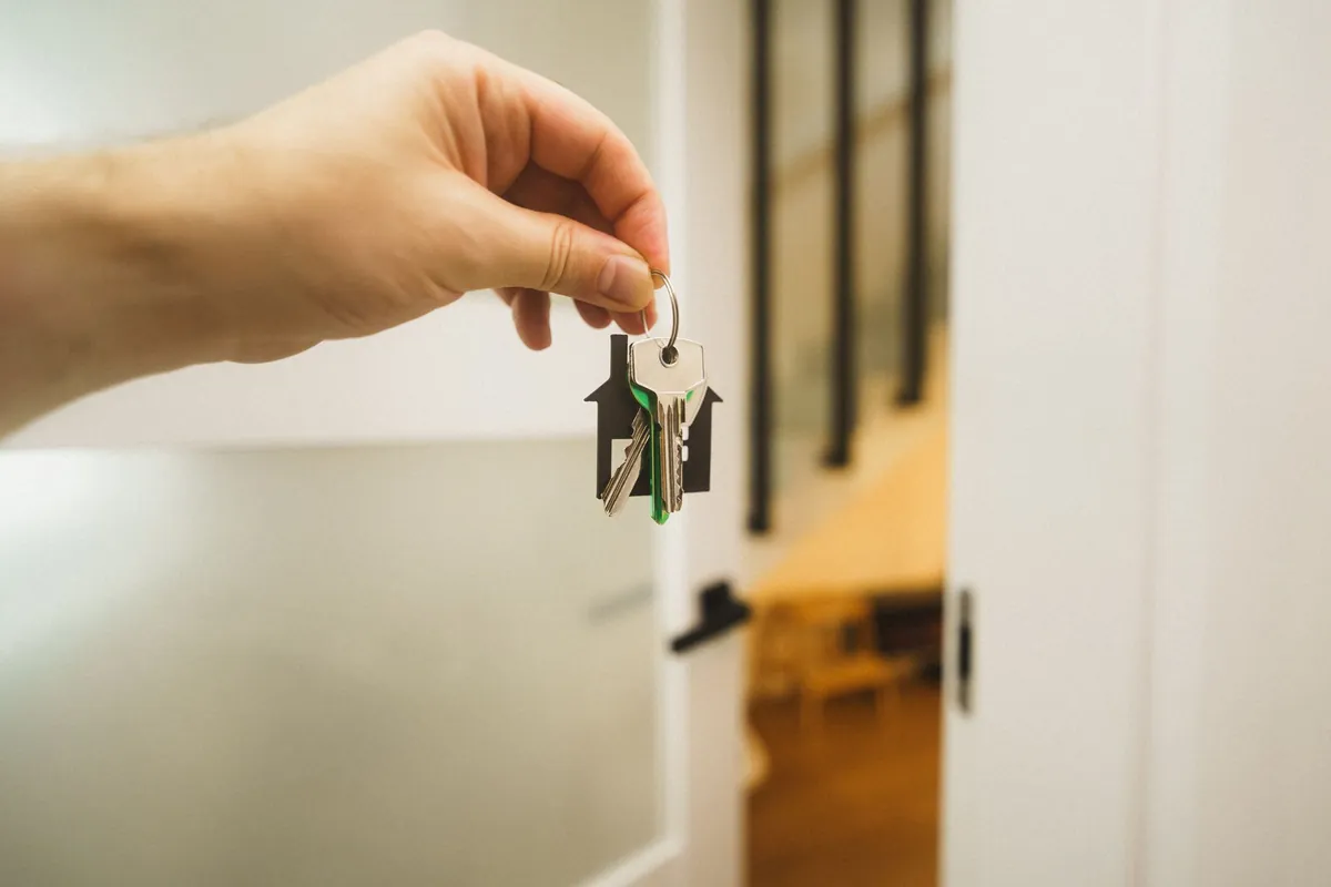 A hand holding house keys on a house-shaped key ring at an open door