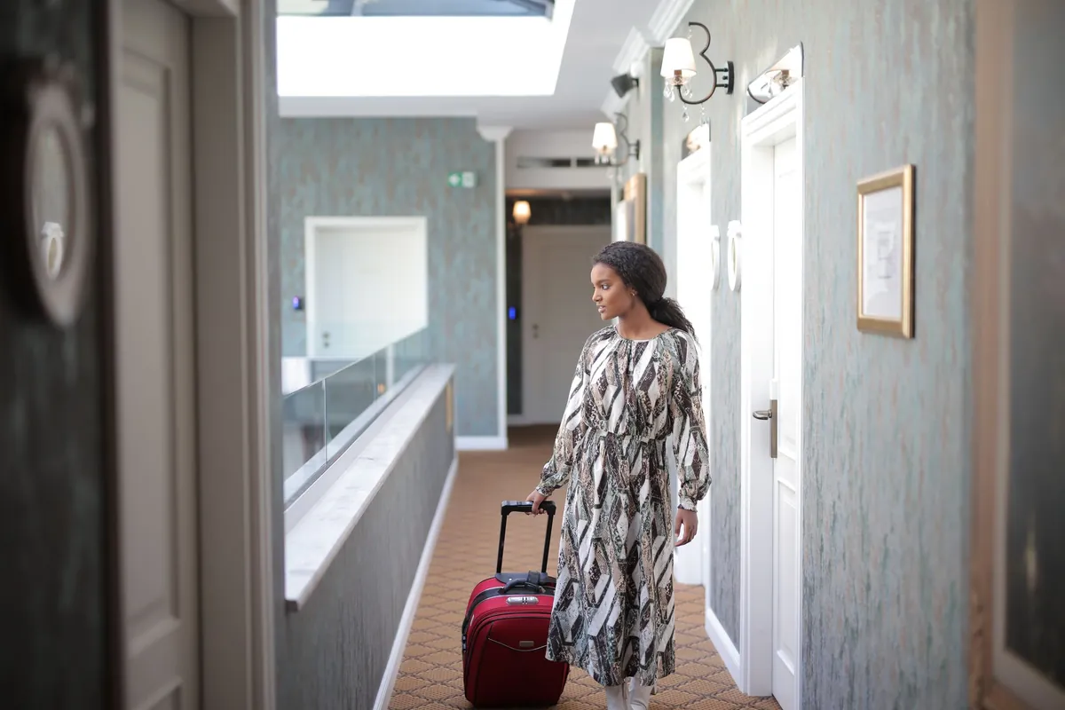 A guest wheeling a suitcase along a bright hallway towards a door