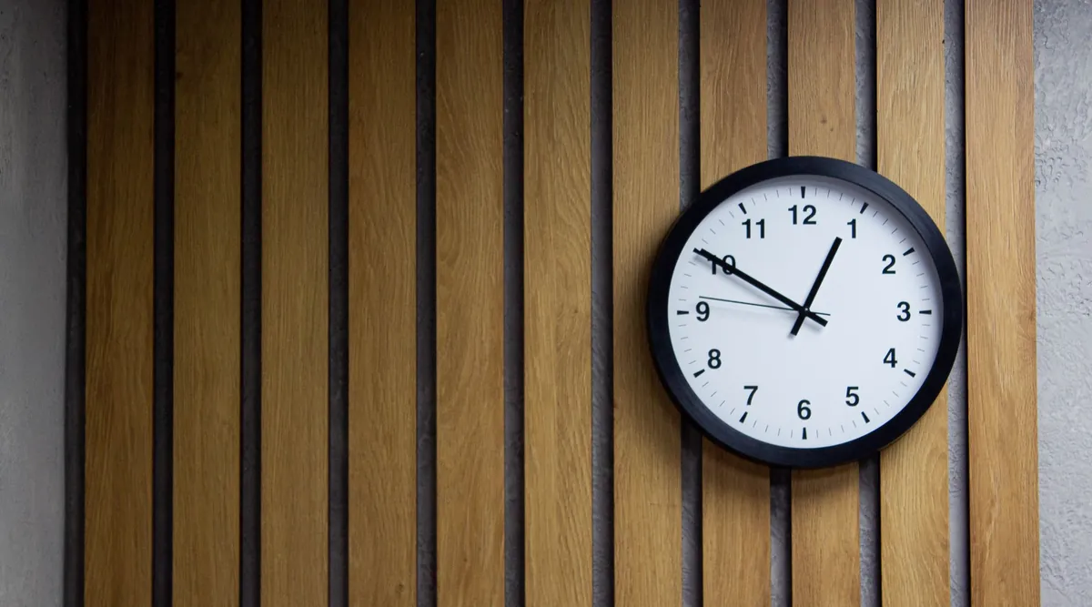 A round black wall clock mounted on vertical wooden slats