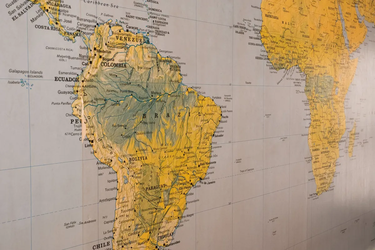 A close-up of a printed wall map showing South America in yellow and green with the west coast of Africa at the right edge.