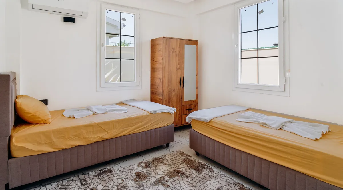 Two single beds made up with towels in a bright bedroom with a wooden wardrobe