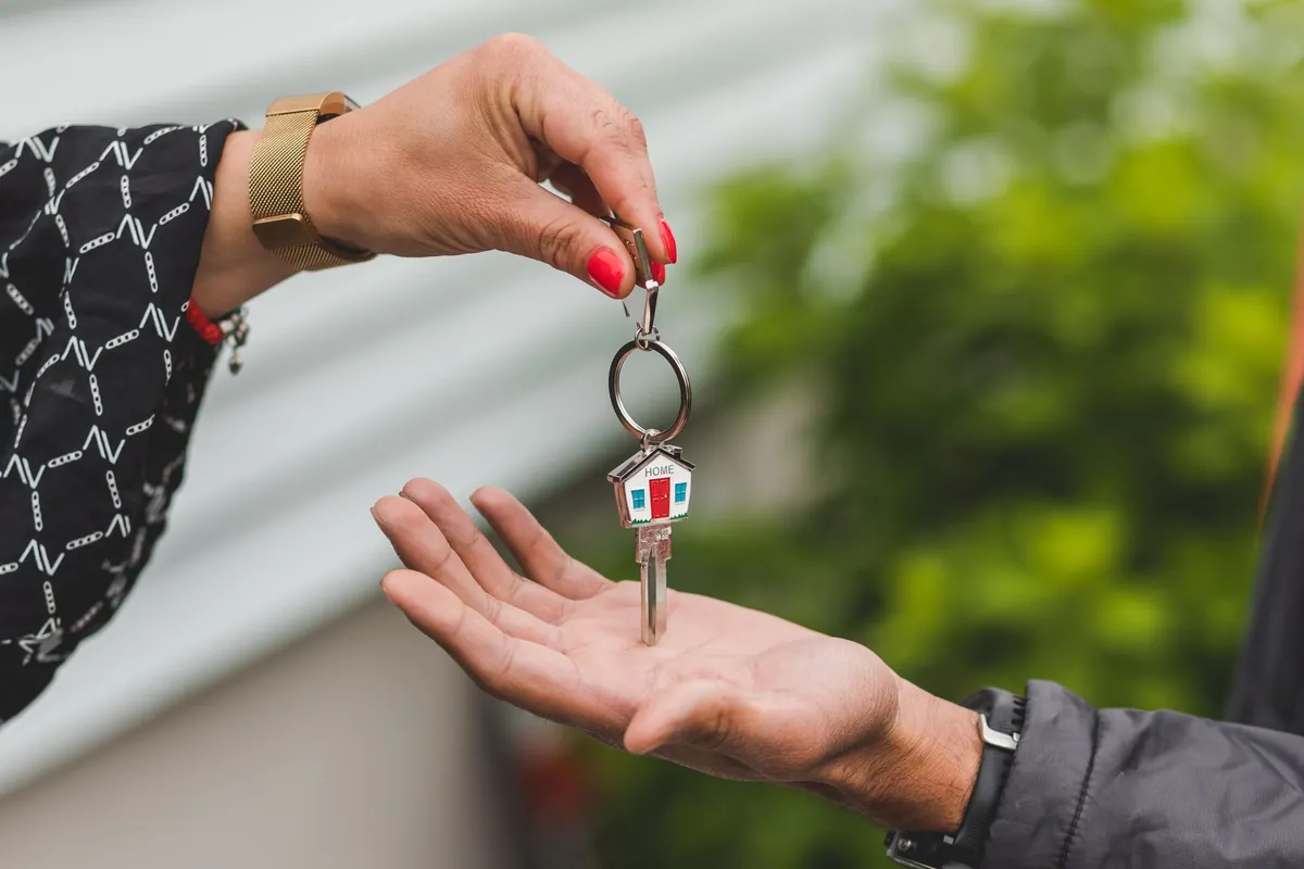 A host dropping a house key on a small house-shaped key ring into a guest's open hand