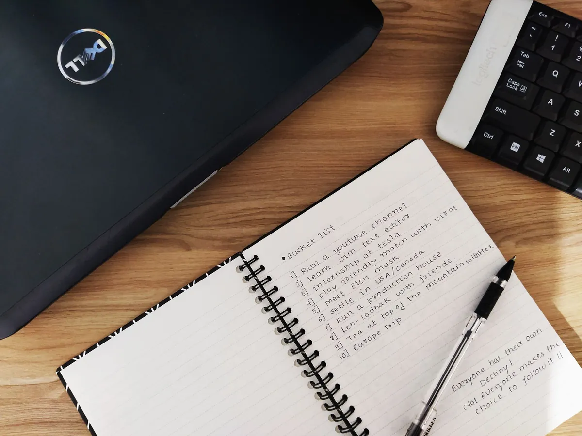 An open notebook with a handwritten list beside a closed laptop