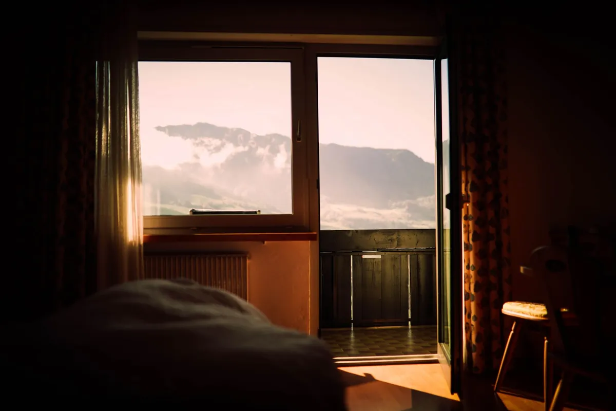 An unmade bed in a dim room with evening light through the window