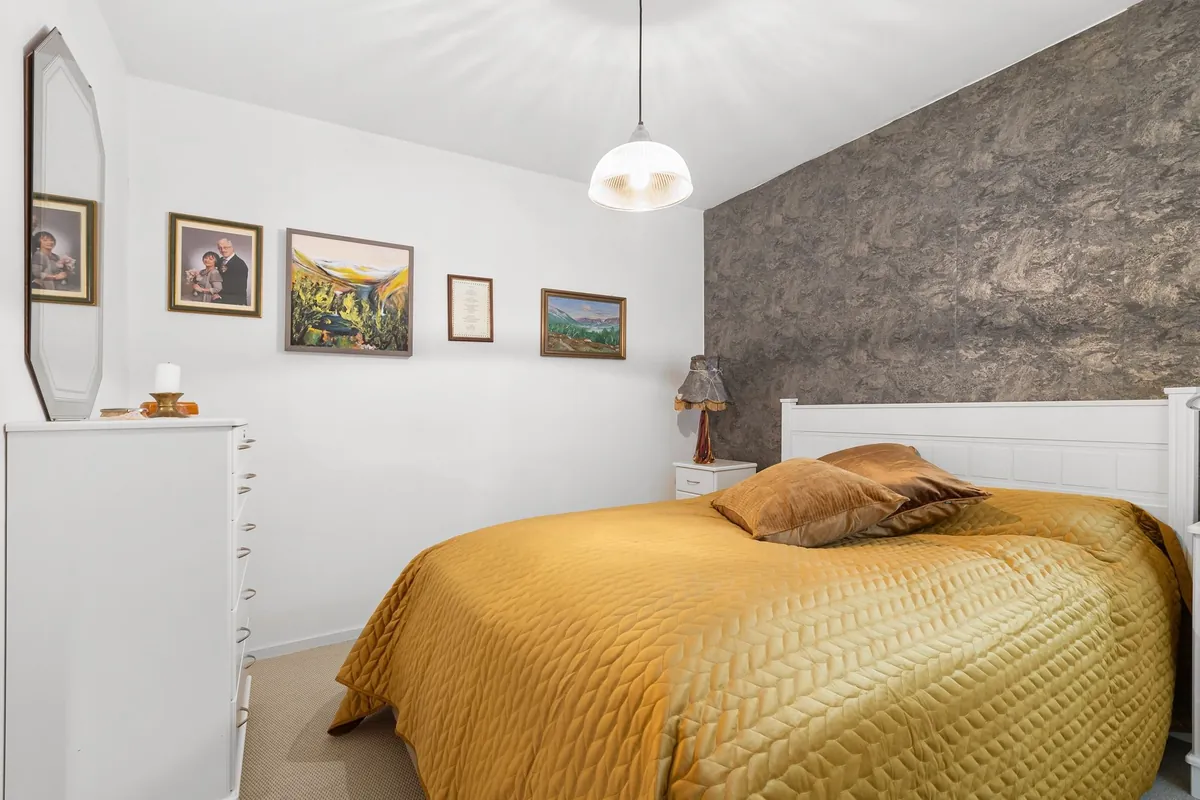 A bright bedroom with a yellow bedspread, framed pictures and a pendant lamp
