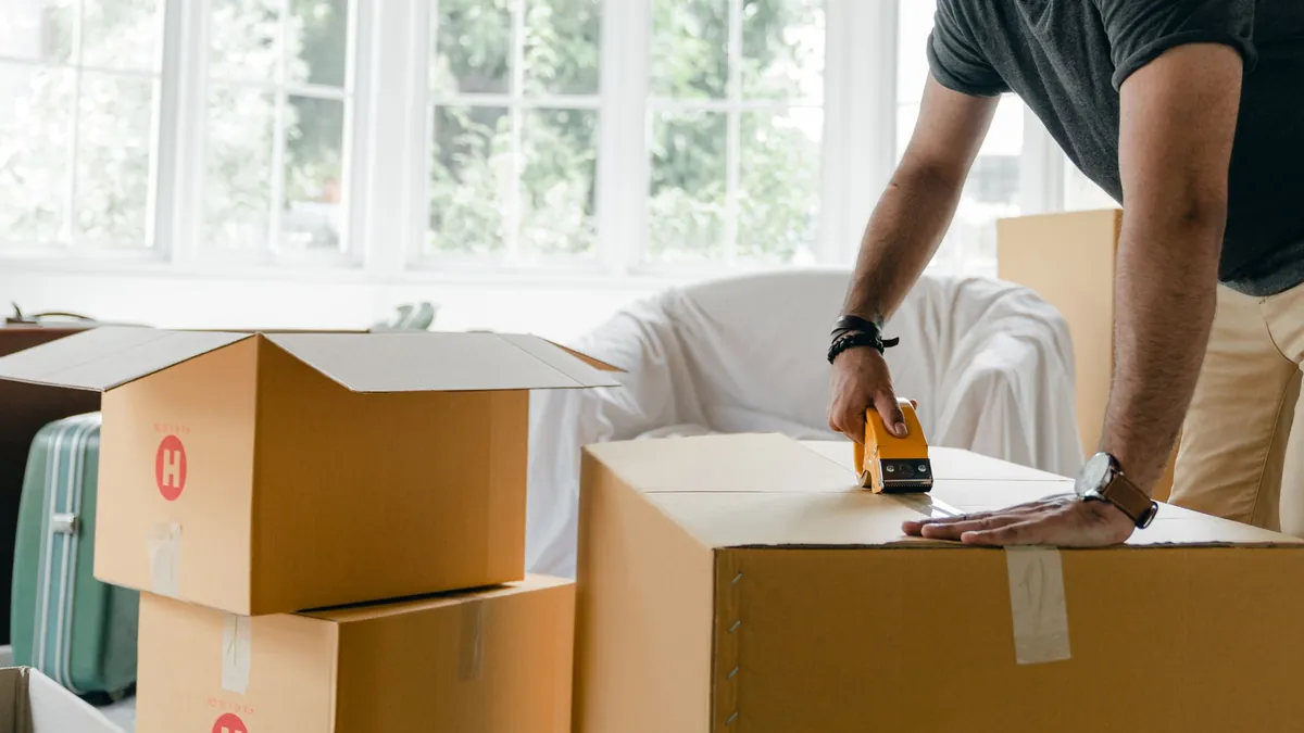A man in casual clothes taping a cardboard box closed