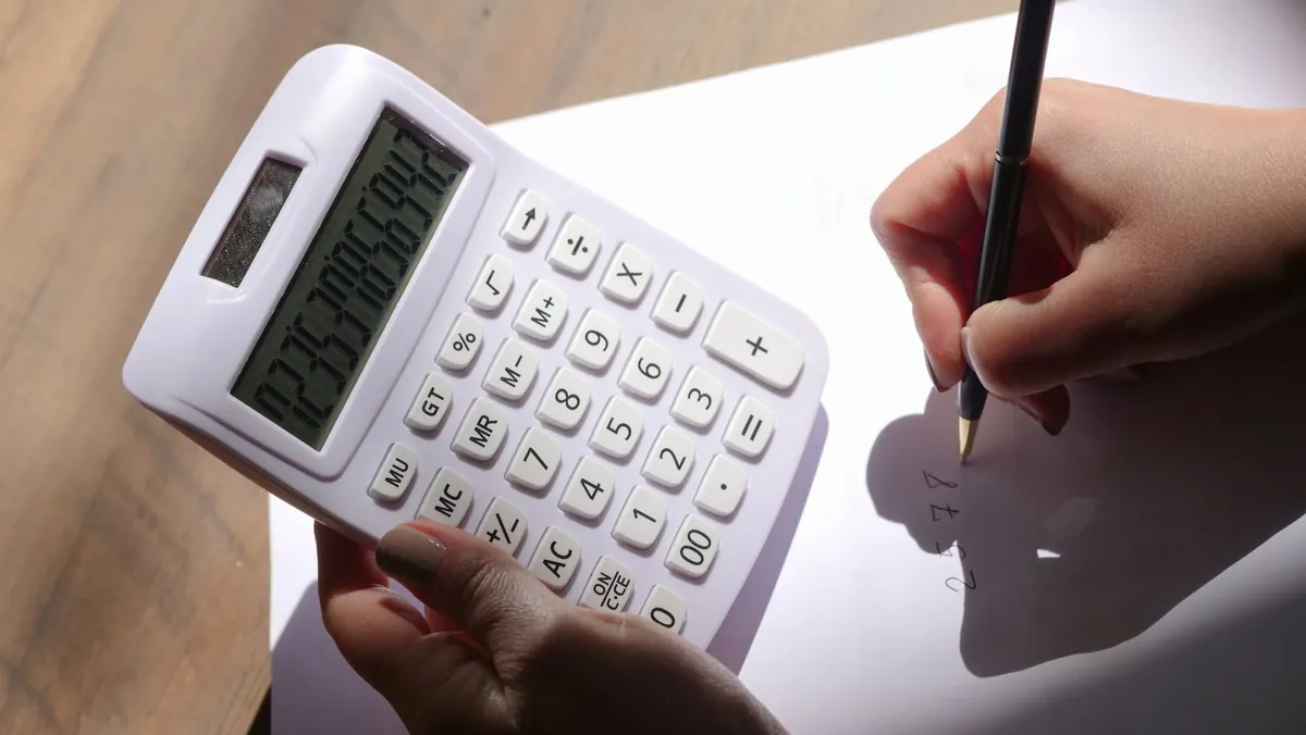 Two hands, one holding a calculator and one writing on a sheet of paper
